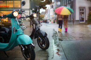 dos scooters electricas y mujeres bajo la lluvia